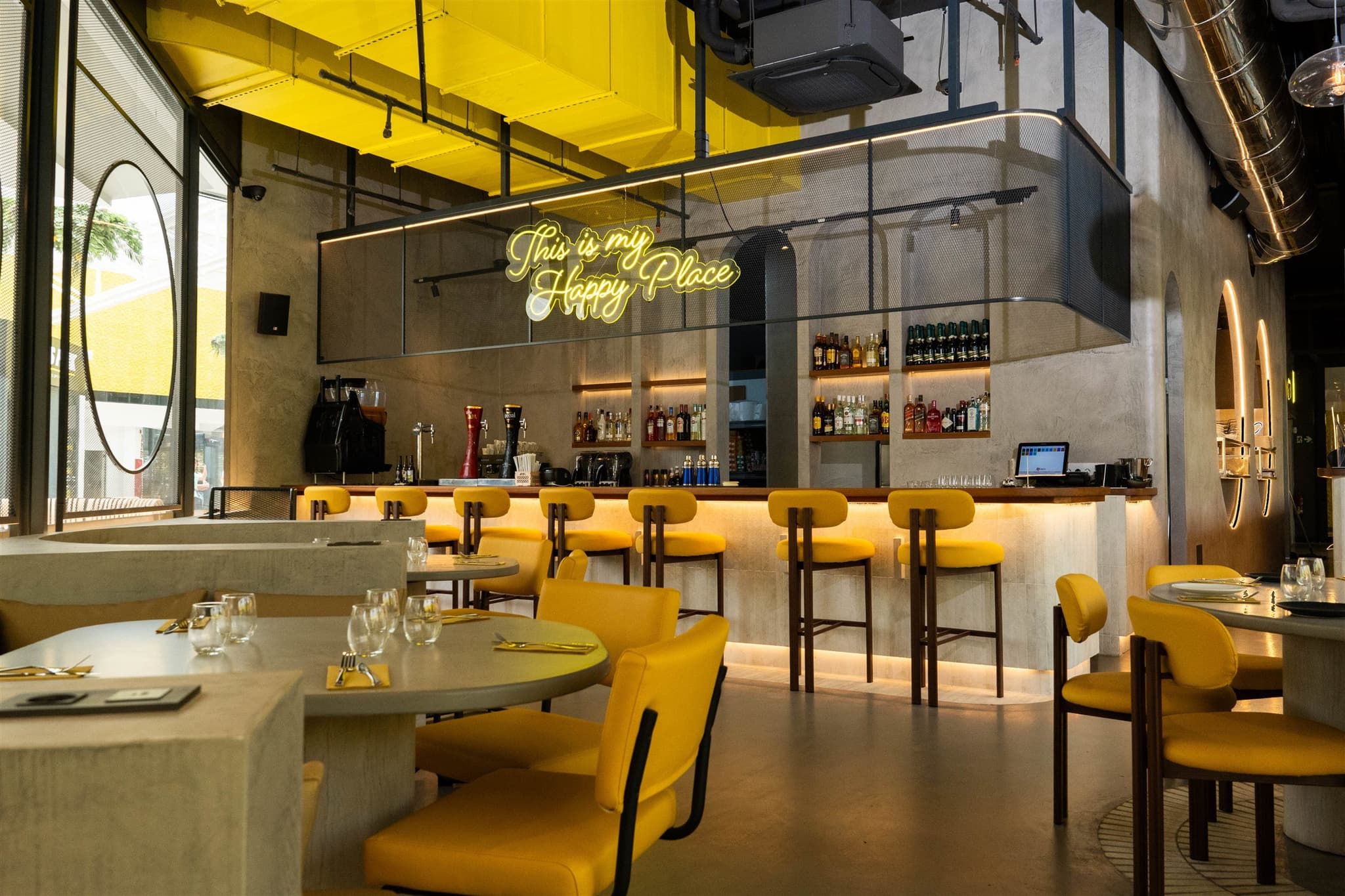 Barra de Dedos La Gran Manzana con el rótulo de neón «This is my Happy Place» y taburetes tapizados en amarillo