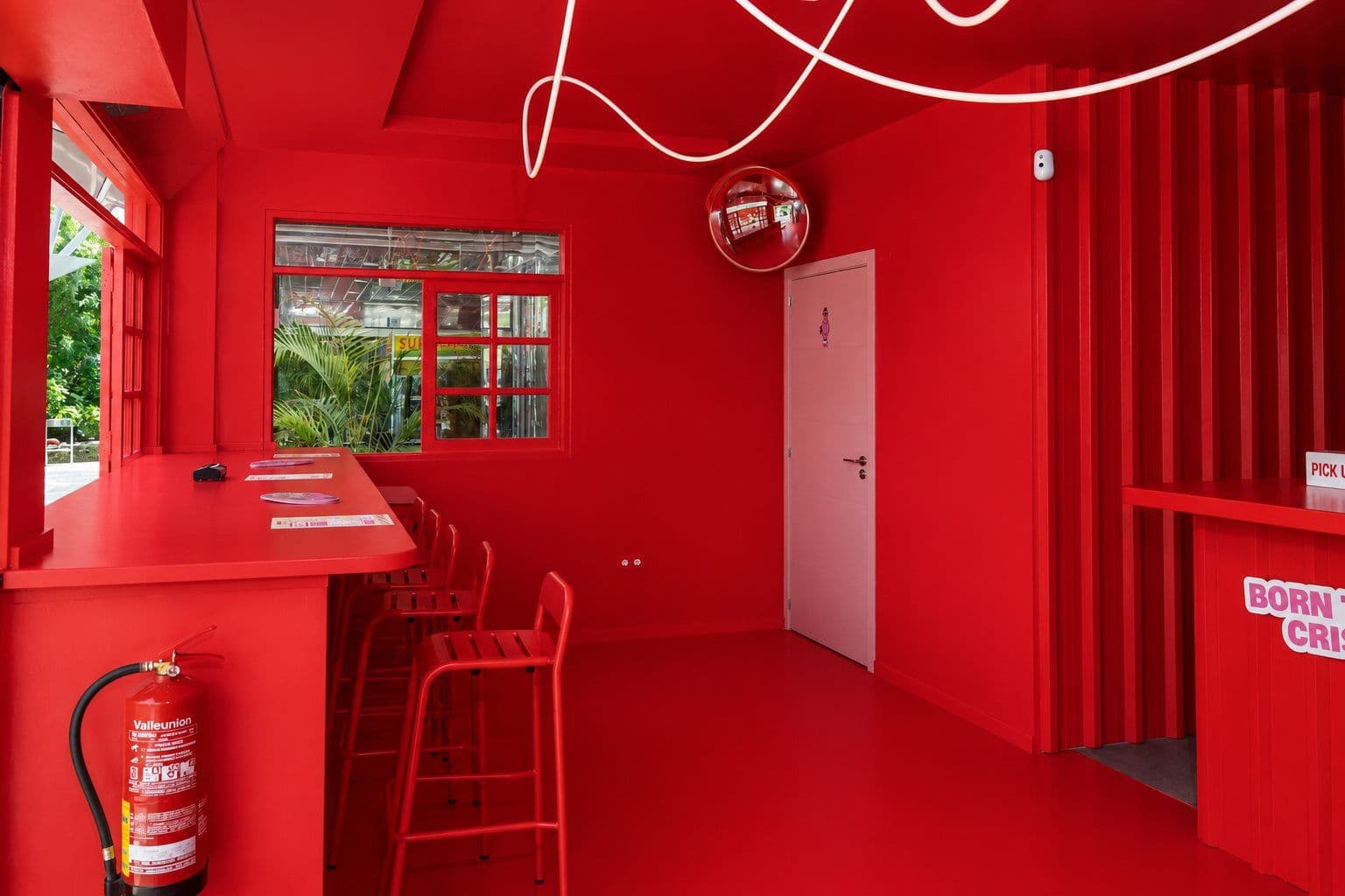 Interior de Crispins con barra alta junto al ventanal, taburetes rojos y neón perimetral