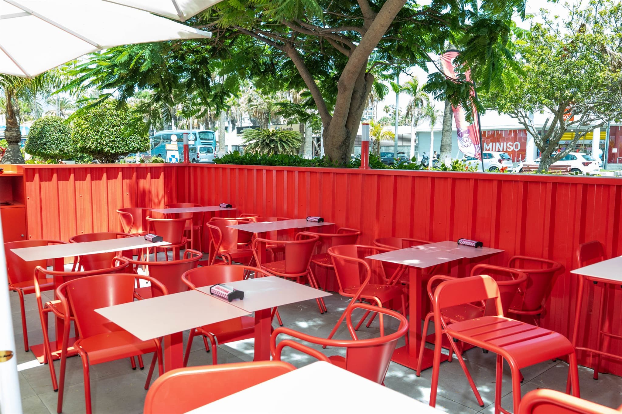 Terraza de Crispins bajo sombrillas blancas, con el cerramiento rojo de chapa perfilada
