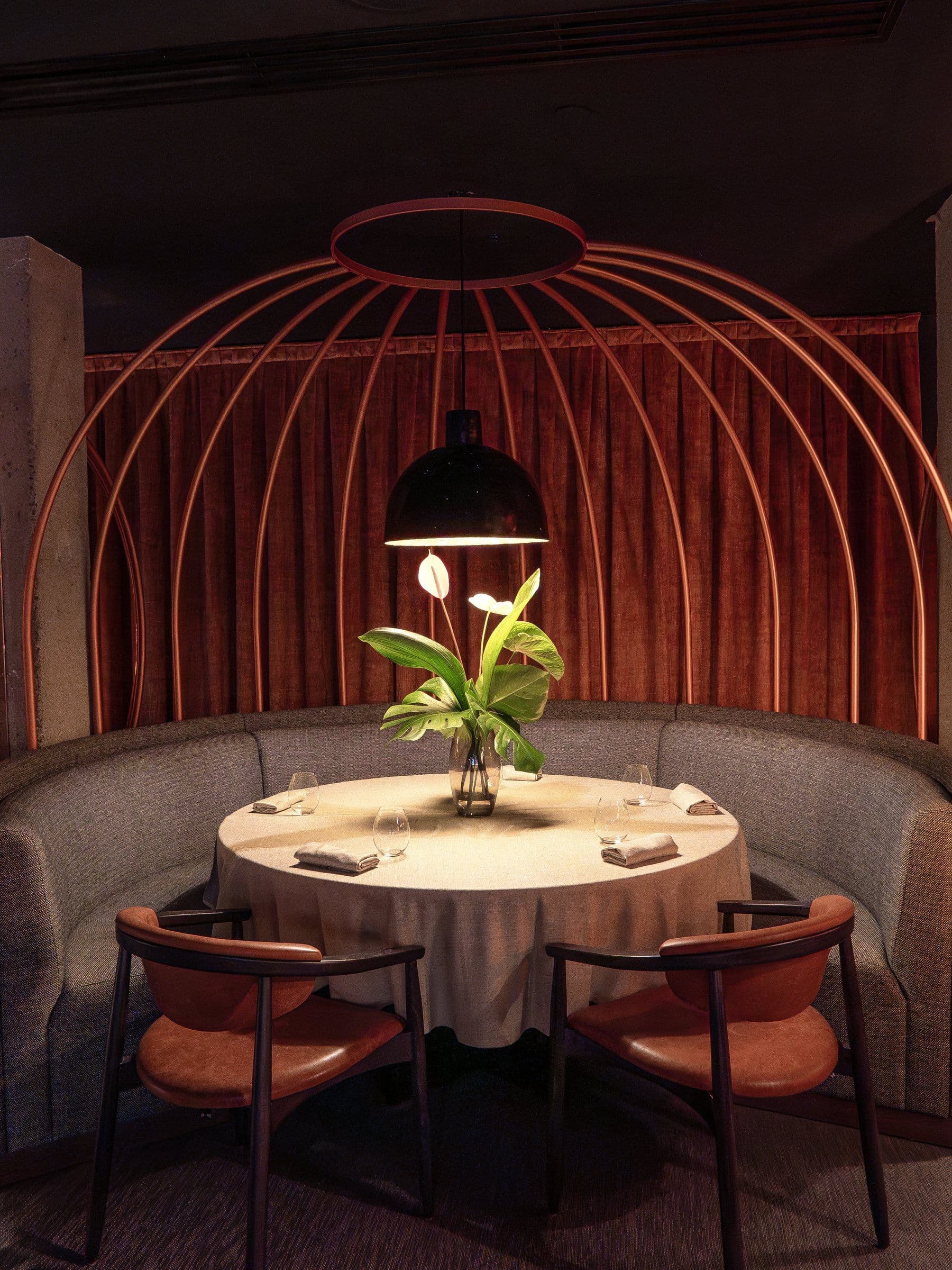 Reservado circular de Char Fuego y Brasas bajo una cúpula de varillas metálicas, con banco curvo tapizado y mesa redonda vestida