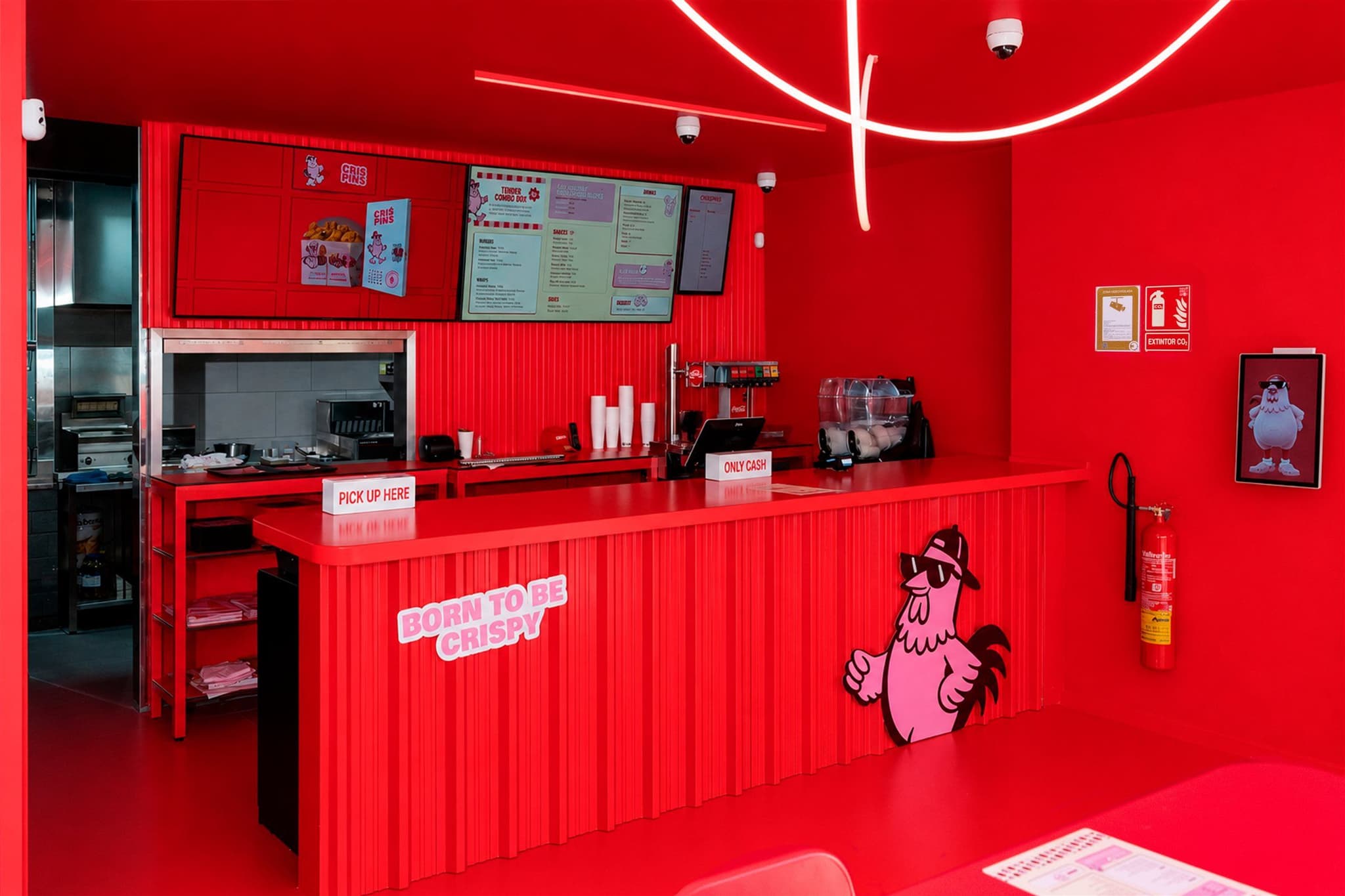 Mostrador de pedido de Crispins en rojo, con la cocina a la vista al fondo y las pantallas de carta sobre el frente